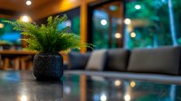 Decorative fern plant in black textured pot on reflective surface with blurred modern restaurant interior, soft bokeh lights and cozy seating area background.