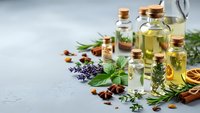 Essential oils in glass bottles with fresh herbs and spices on gray background for aromatherapy, natural wellness and organic skincare products.