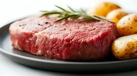 Raw beef steak with fresh rosemary sprig and baby potatoes on gray ceramic plate against white background. Close up view of premium cut meat for cooking.