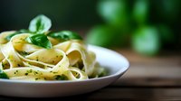 Fresh fettuccine pasta with herbs and olive oil served on white plate, selective focus on foreground with blurred background creates appetizing mood.
