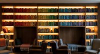 Modern home library interior with colorful books organized by color on wooden shelves, cozy reading chairs and warm lighting for study space design.