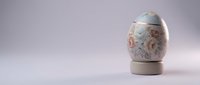 Elegant porcelain Easter egg with delicate floral patterns on wooden stand against soft gradient background for spring holiday decorations and celebrations.