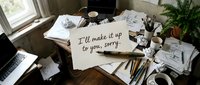 Handwritten apology note on a cluttered artist desk with sketches, crumpled paper, and paintbrushes, conveying regret and creative chaos.