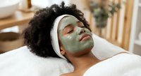 Young African American woman relaxing with green clay facial mask at spa, enjoying skincare treatment for healthy glowing skin and wellness routine.