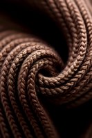 Twisted brown rope in macro photography showing detailed texture and intricate knot pattern against dark background, creating dramatic lighting effect.