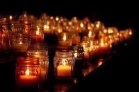 Row of glowing candles in glass jars creating warm atmospheric lighting against dark background, perfect for memorial or spiritual events.