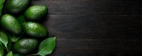 Fresh green avocados with leaves arranged on dark wooden background, top view with copy space for text. Food photography layout.