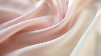 Soft, flowing fabric in blush pink and cream tones with gentle waves and folds, suitable for fashion, textile, and luxury product backgrounds.