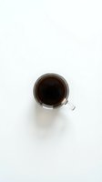 Glass mug filled with black coffee on white background, top view. Morning beverage, caffeine drink for breakfast and energy boost in minimalist style.