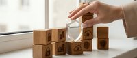 Professional woman hand placing magnifying glass over wooden blocks with business icons for strategic analysis and planning concepts.