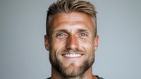 Confident Caucasian man with bright smile, styled blonde hair and neat beard against gray background. Professional headshot for business, lifestyle and dental marketing.