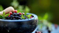 Fresh mixed berries in ceramic bowl with mint leaves on outdoor table for healthy breakfast and organic food concepts.