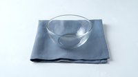 Empty glass bowl on blue linen napkin, isolated on white background. Suitable for kitchenware, tableware, dining, and food styling design projects.