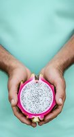 Male hands holding sliced dragon fruit with white flesh and black seeds against turquoise background. Suitable for food, nutrition, healthy eating, and wellness content.