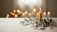 Burning candle with eucalyptus branches on white surface against warm bokeh lights background creating cozy atmospheric holiday mood for relaxation.