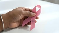 Hand holding pink ribbon symbol for breast cancer awareness campaign and women health support on white background.