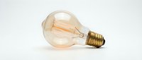 Vintage incandescent bulb with warm glowing filament and brass base isolated on white background, suitable for lighting design, retro decor, and energy concept projects.