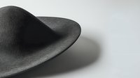 Black wide-brimmed felt hat casting dramatic shadow on white surface, minimalist fashion accessory photographed in monochrome style with selective focus.