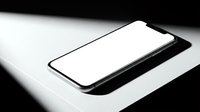 Modern smartphone with blank white screen lying on white surface with dramatic black and white lighting for mockup and app presentation designs.