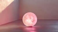 Glowing pink moon lamp casting soft reflections on glossy surface in minimalist interior setting with dramatic shadows and ambient lighting effects.