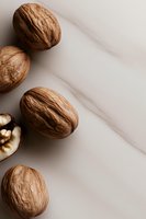 Whole walnuts and half walnut kernel on marble background in minimal composition, natural light creates soft shadows for food photography and packaging design.