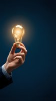 Hand holding illuminated incandescent bulb against dark blue background, representing innovation, creativity, ideas, and business solutions for corporate and entrepreneurial concepts.