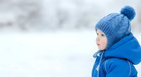 Young child wearing blue knit beanie and winter jacket, gazing thoughtfully at snowy landscape. Suitable for winter campaigns, seasonal marketing, and family-oriented designs.