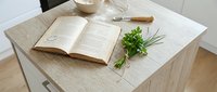 Open book with fresh green herbs and writing tools arranged on light wooden desk surface, suitable for lifestyle, wellness, cooking, and educational content.