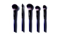 Professional makeup brushes with black and purple bristles on dark handles arranged in row against white background, isolated cosmetic tools for beauty application.