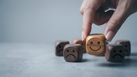 Hand picking wooden cube with smiley face among sad faces, customer satisfaction and positive mindset concept for business.