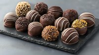 Assorted chocolate truffles with different toppings and decorative stripes arranged on dark slate board, luxury handmade confectionery close up shot in natural light.