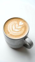 Overhead view of cappuccino with latte art leaf design in gray ceramic mug on white surface, suitable for coffee shop menus and beverage marketing.