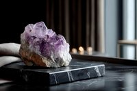 Raw amethyst crystal cluster on black marble surface with soft window light creating serene atmosphere for spiritual practices and home decor.