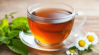 Fresh herbal tea in transparent glass cup with mint leaves and chamomile flowers on wooden surface, aromatic hot beverage for relaxation and wellness.