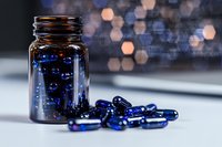 Blue transparent capsules and amber glass bottle on white surface with blurred bokeh background, medical supplement concept for pharmacy and healthcare.