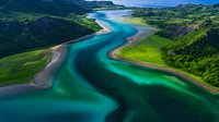 Aerial view of winding turquoise river flowing through green mountain valley landscape, with sandy shores and crystal clear water creating natural patterns.