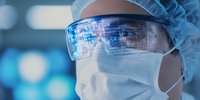 Healthcare professional wearing protective equipment with digital data reflection in safety goggles during medical procedure in hospital environment.