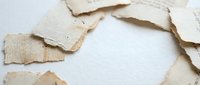 Torn aged paper pieces scattered around white background creating vintage frame with copy space for text and design projects.