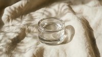 Empty glass jar on neutral fabric with natural sunlight casting shadows, suitable for product mockups, skincare packaging, cosmetics branding, and lifestyle photography.