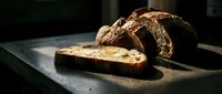Freshly baked artisan bread loaf with crusty exterior and soft interior slice on dark surface, ideal for bakery, food, and culinary content.