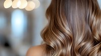 Luxurious wavy brown hair with blonde highlights and balayage technique shown in close-up on blurred bokeh background. Professional hairstyling and coloring result.