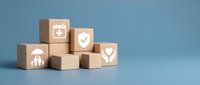 Wooden blocks with insurance and healthcare icons including family protection, calendar, shield, and heart care symbols on blue background.