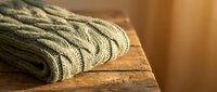 Cozy knitted cable sweater in warm olive green folded on rustic wooden surface with soft natural lighting for autumn winter fashion and textile concepts.