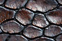 Extreme close up of dark brown leather texture with hexagonal pattern and deep cracks showing natural wear and aged surface detail.