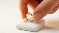 Hand holding a gold diamond engagement ring above a white velvet jewelry box, symbolizing proposal, love, and luxury gift giving.