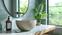 Modern concrete vessel sink on wooden countertop with round mirror, amber glass dispenser and green plants in bright bathroom interior. Natural spa decor.