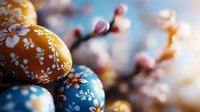 Decorated Easter eggs with floral patterns in blue and yellow colors against blurred spring cherry blossoms background creating festive holiday atmosphere.