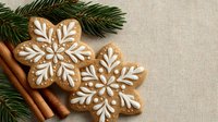 Festive gingerbread snowflake cookies with white icing decoration, cinnamon sticks and pine branches on neutral linen background.