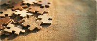 Wooden jigsaw puzzle pieces scattered on textured surface with warm lighting creating problem-solving and teamwork concept for business presentations.