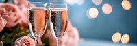 Two champagne flutes filled with sparkling wine against soft bokeh lights and pink roses creating romantic celebration atmosphere for special occasions.